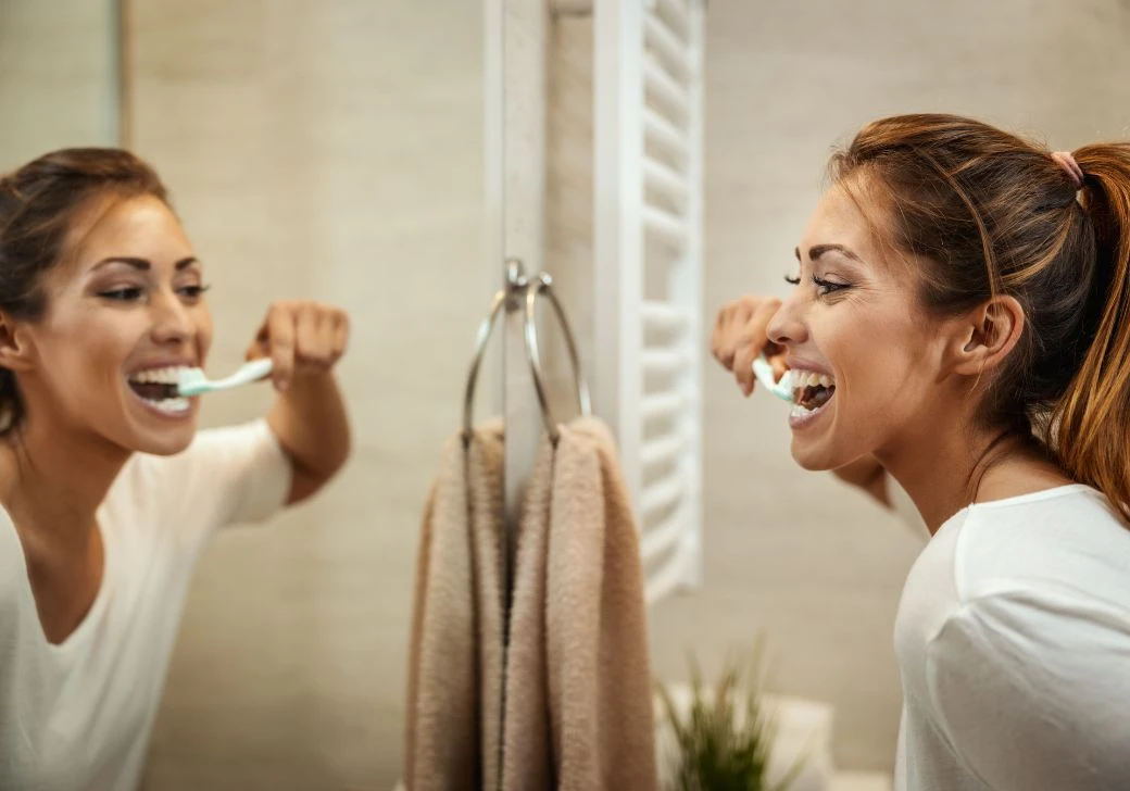 Devojka pere zube pred ogledalom.